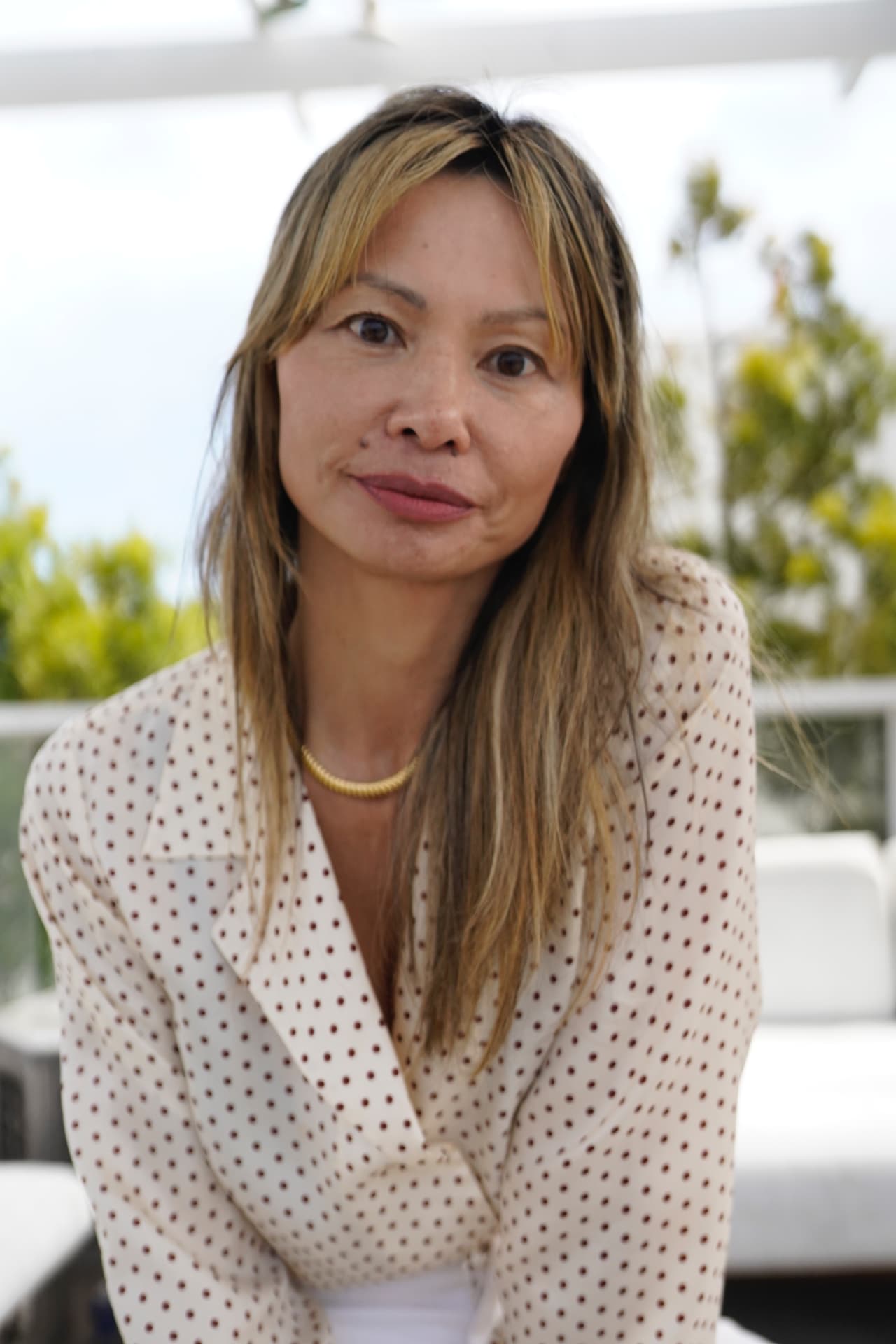 Olivia Corwin, a couples, family, and sex therapist in Santa Monica, looking at the camera on a sunlit patio with greenery behind her